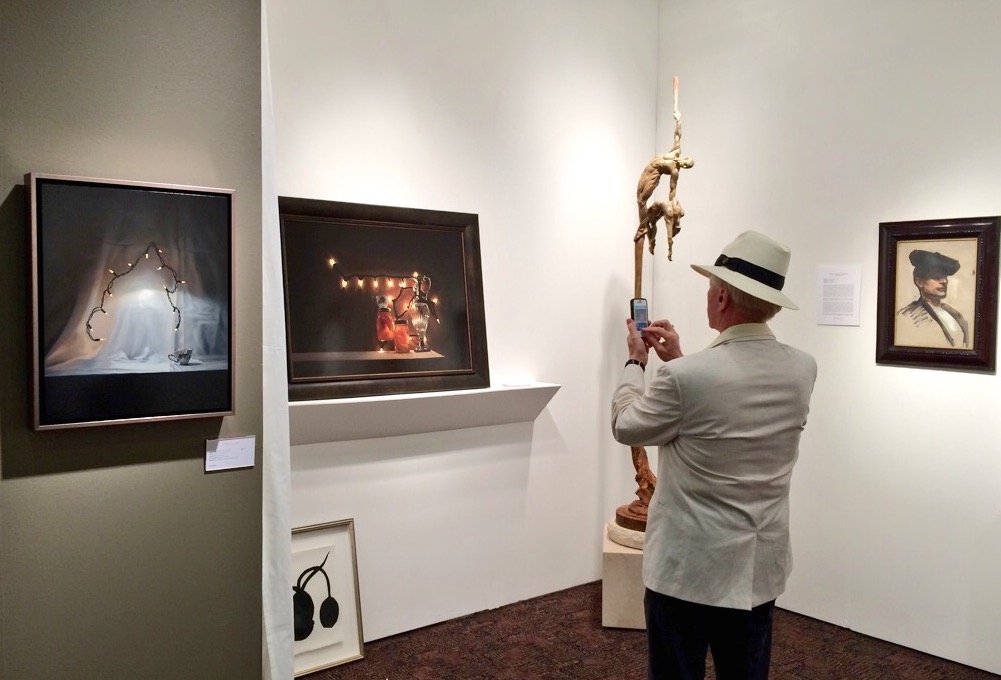 A visitor photographs works by Tom Betts at the Palm Springs Fine Art Fair 2015; installation view of Dawson Cole Fine Art with works by Tom Betts, Donald Sultan, Richard MacDonald, and John Singer Sargent; photo © codylee.co